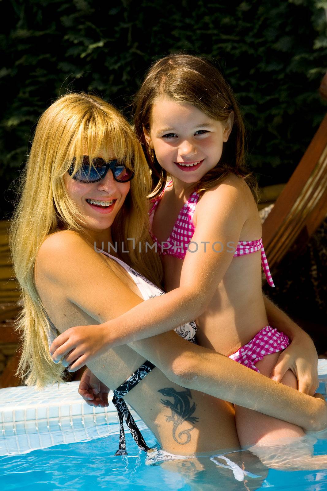 Young blond girl and her sister enjoying the sun in and around the swimming pool