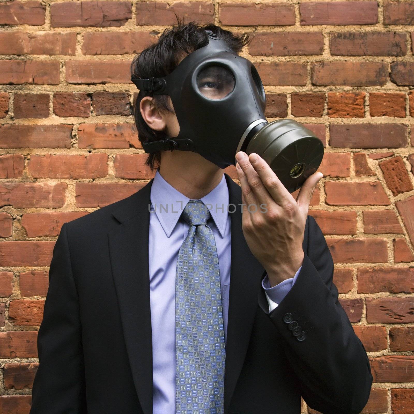 Businessman standing next to brick wall and looking off to side wearing gas mask.