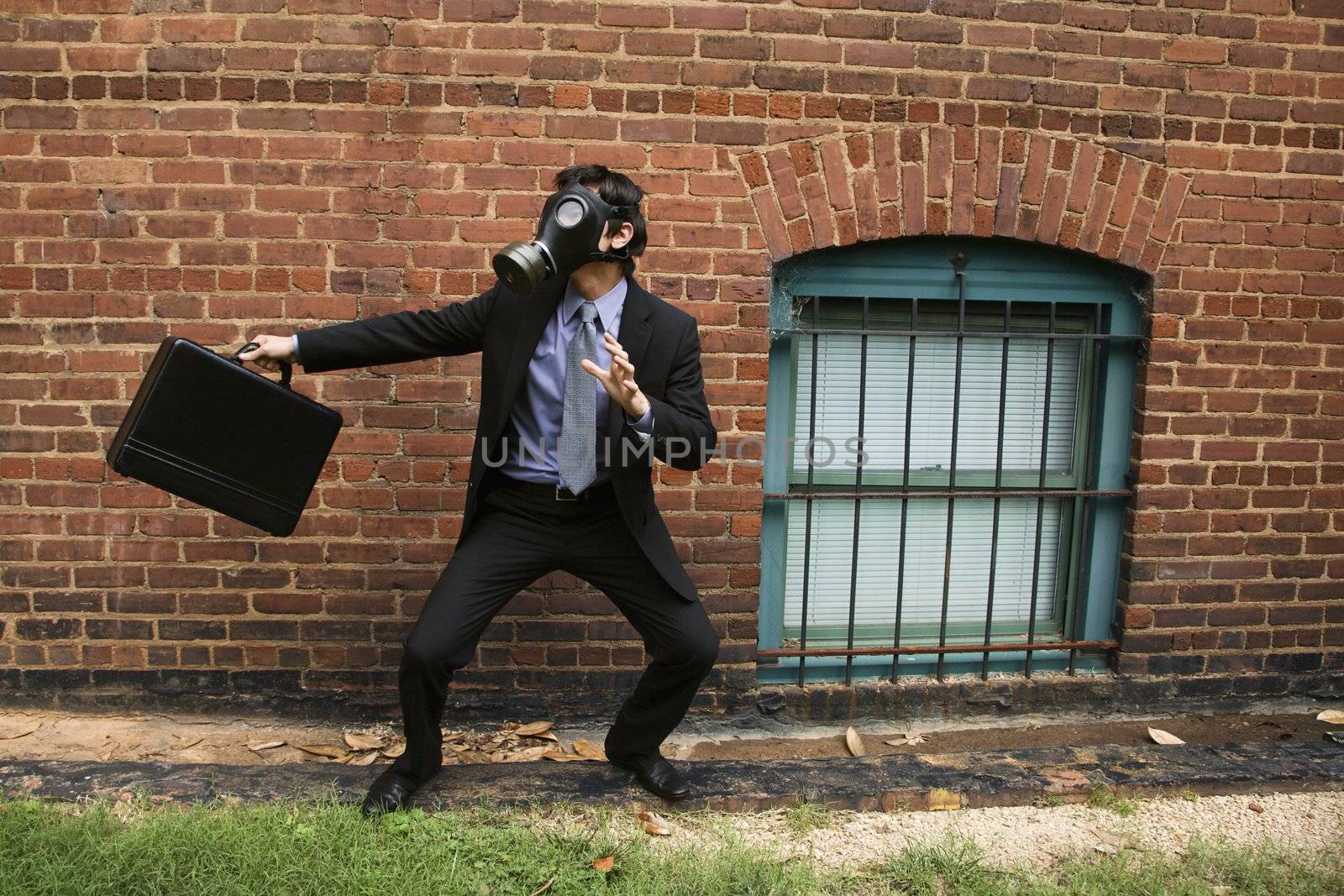 Businessman standing next to brick wall wearing gas mask in fighting stance.