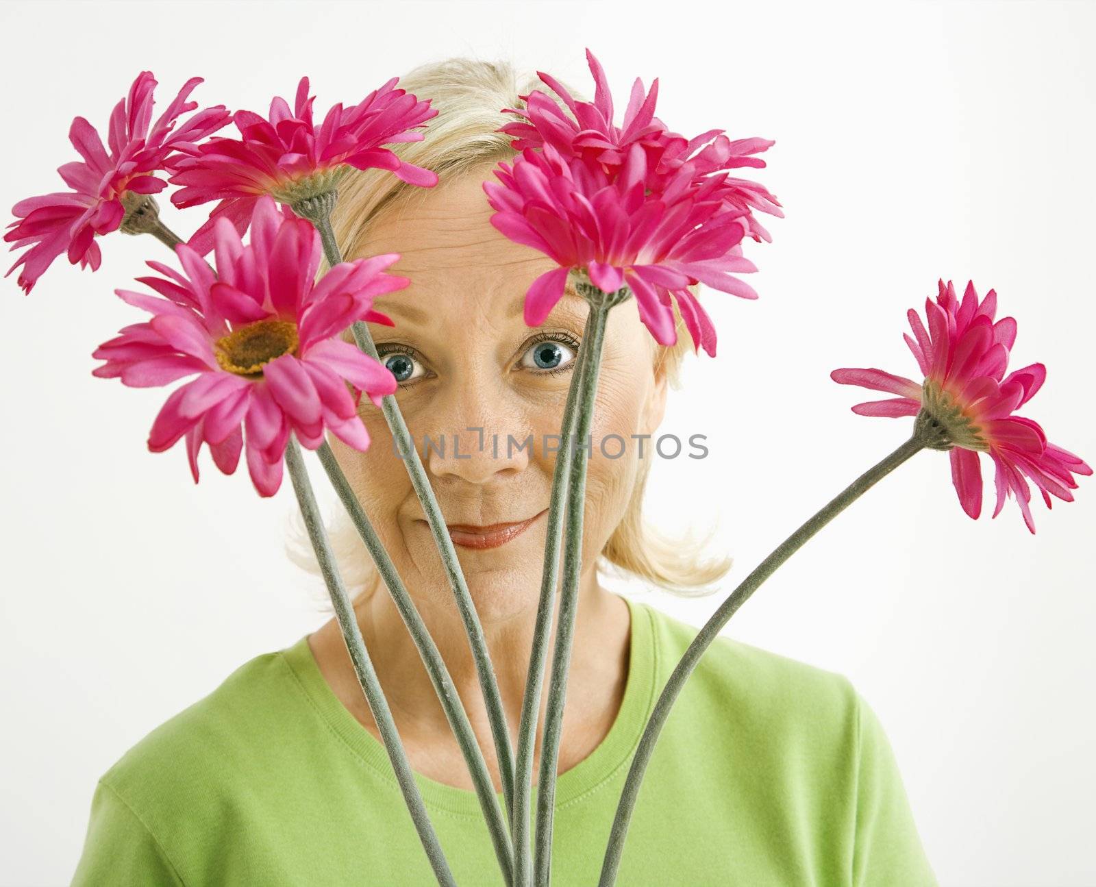 Portrait of smiling adult blonde woman looking through bouquet of pink flowers at viewer.