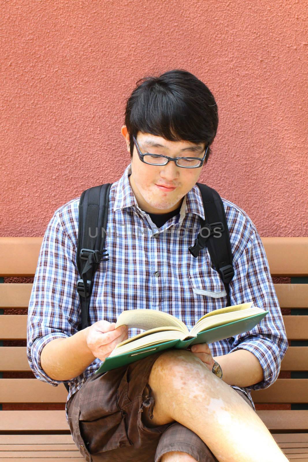 He is reading book on campus.