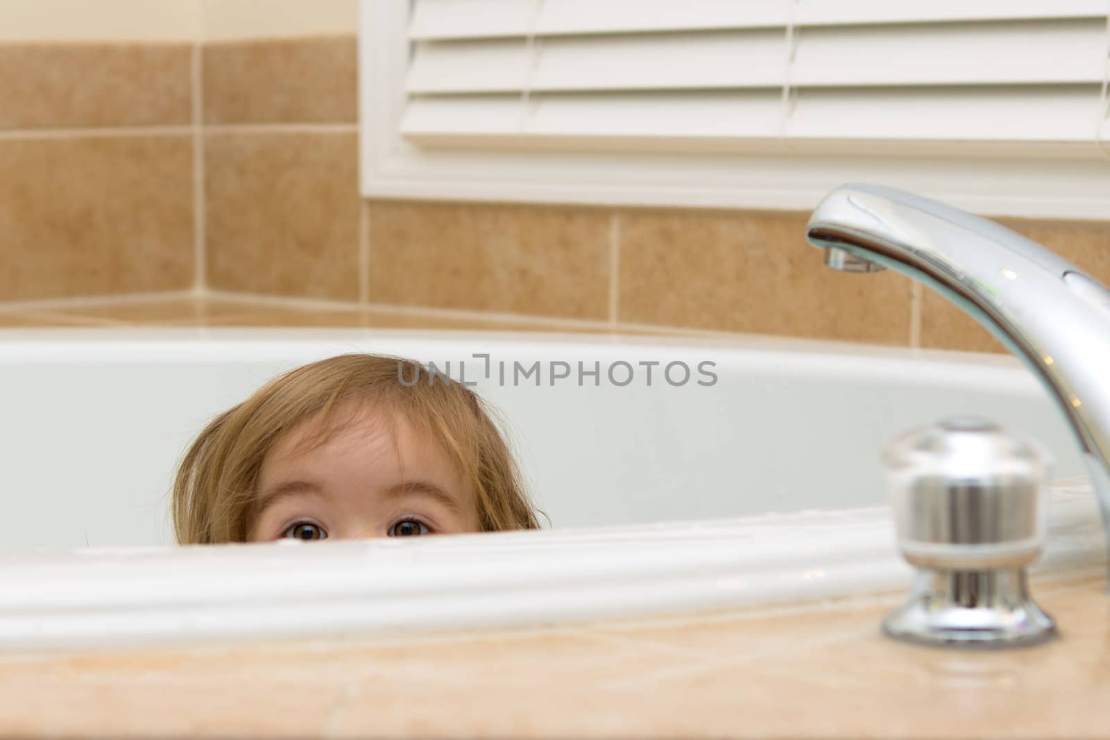 Toddler girl giving curious expression while hiding in the bathtub