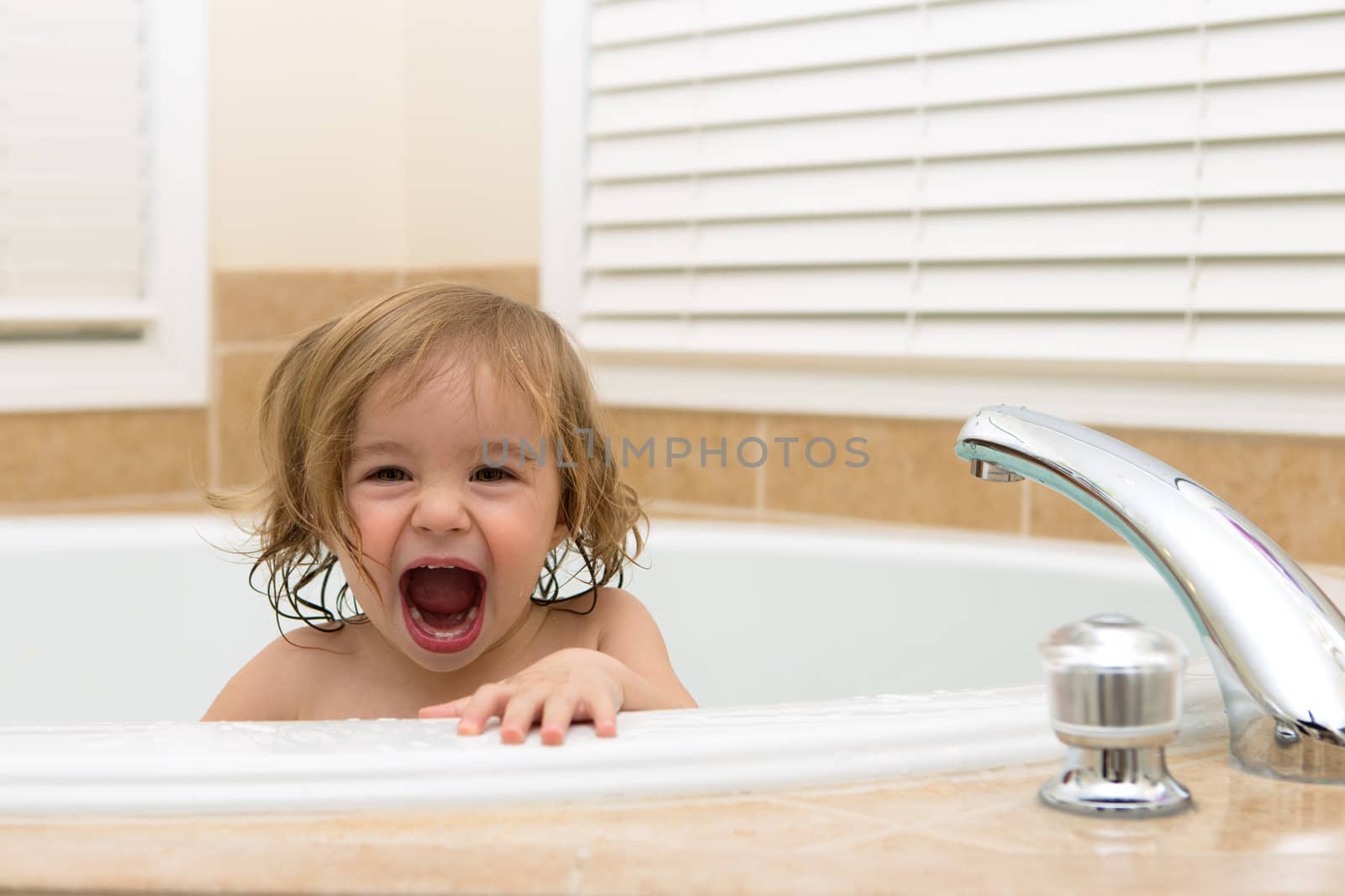 Toddler girl laughing cheerfully her moth open from bath tub. Teething