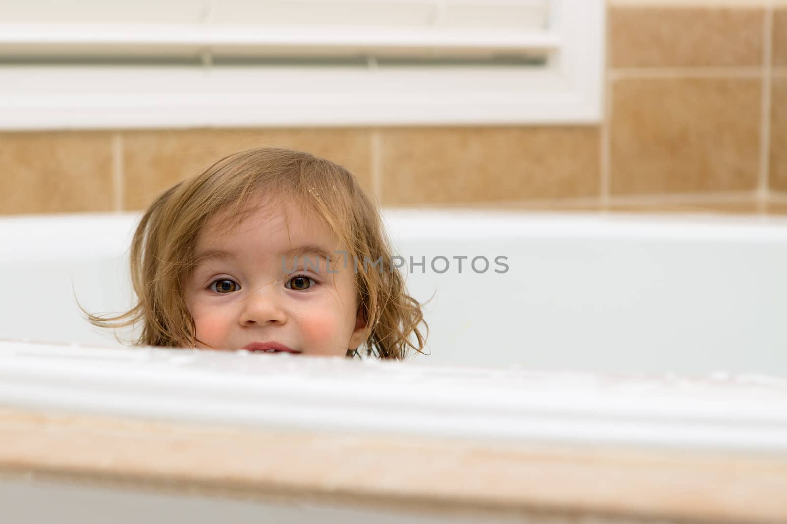 toddler girl giving happy hiding look from the bathtub, perhaps she is looking to take her bath.