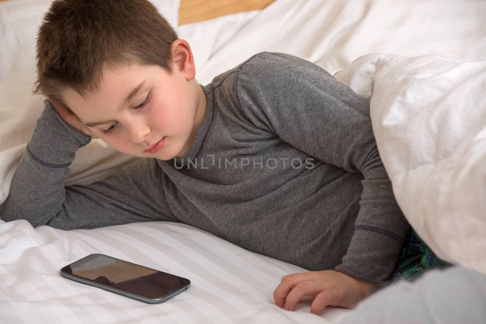 Eight years old kid watching shows on daddy's smart phone before he goes to sleep.