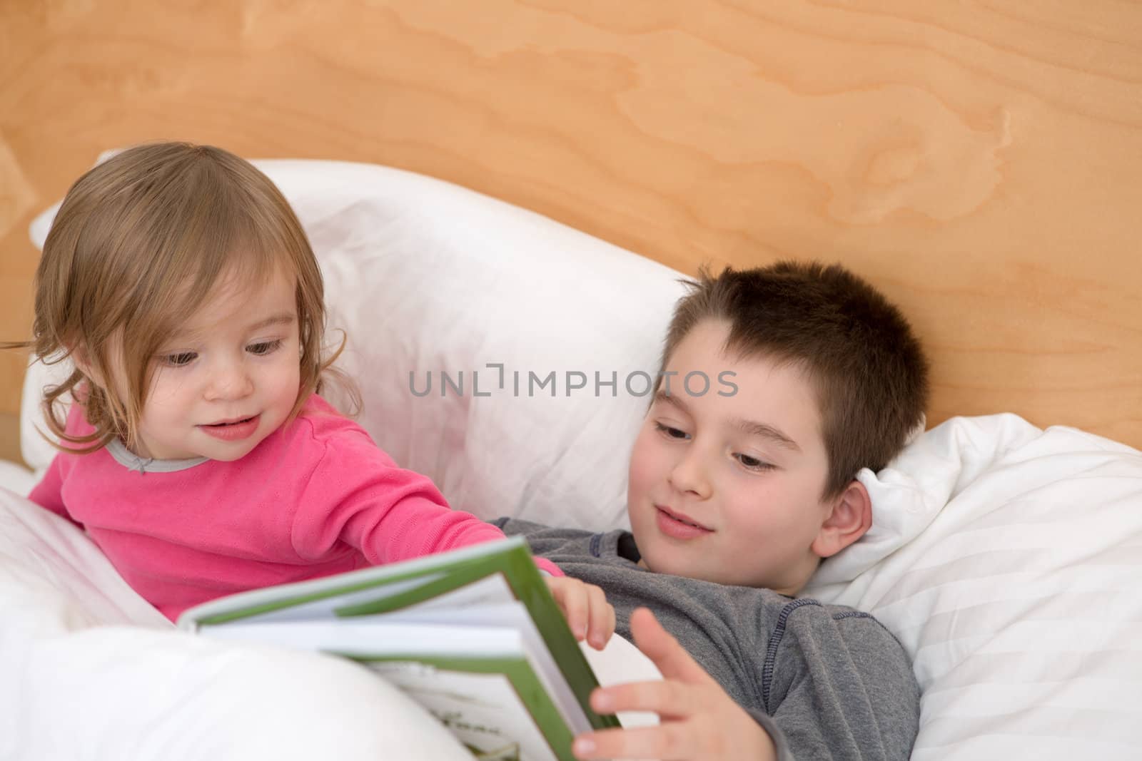 Little sister asking a question to his older brother about a page in the book before they go to sleep.