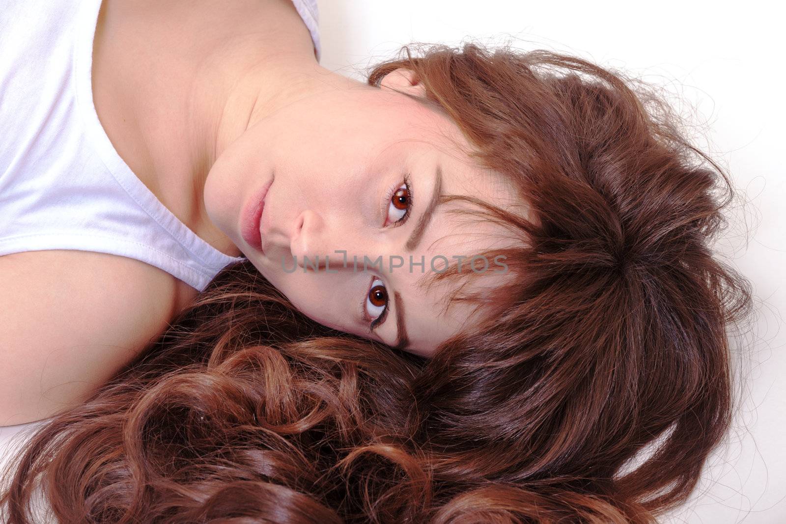 Beautiful serious young woman lying on her back with her lovely curly brunette hair spread around her face looking up at the camera