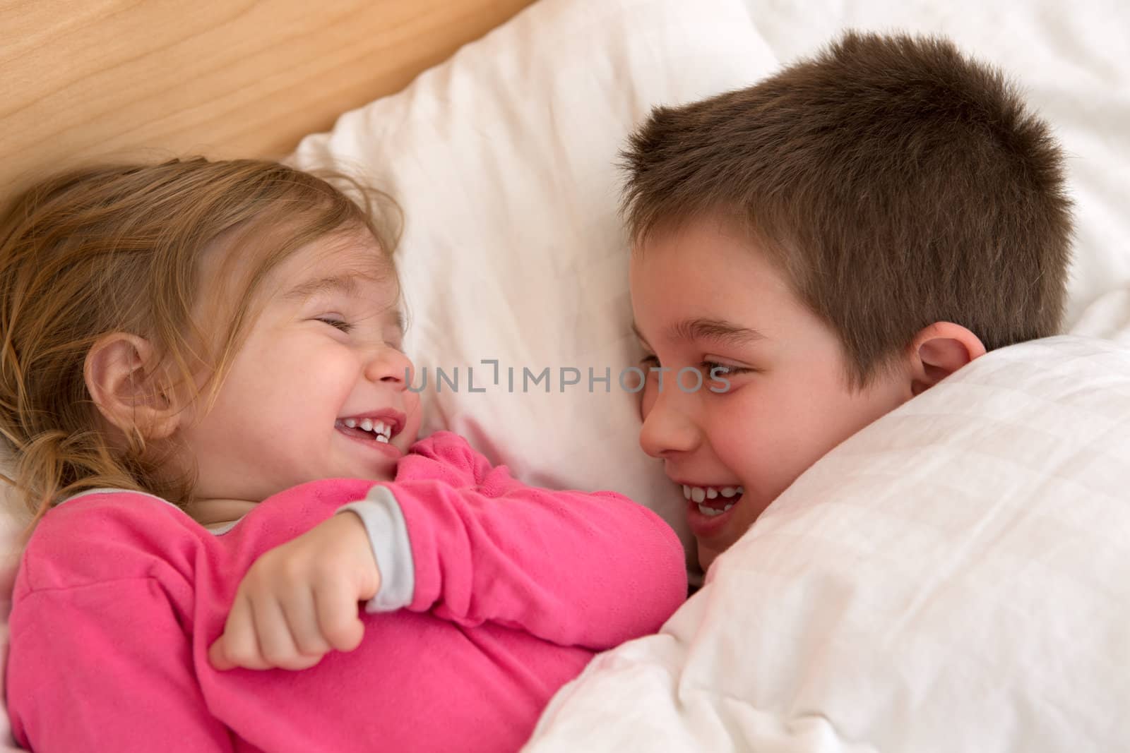 Siblings laughing at each other in the bed, happy cozy moments.