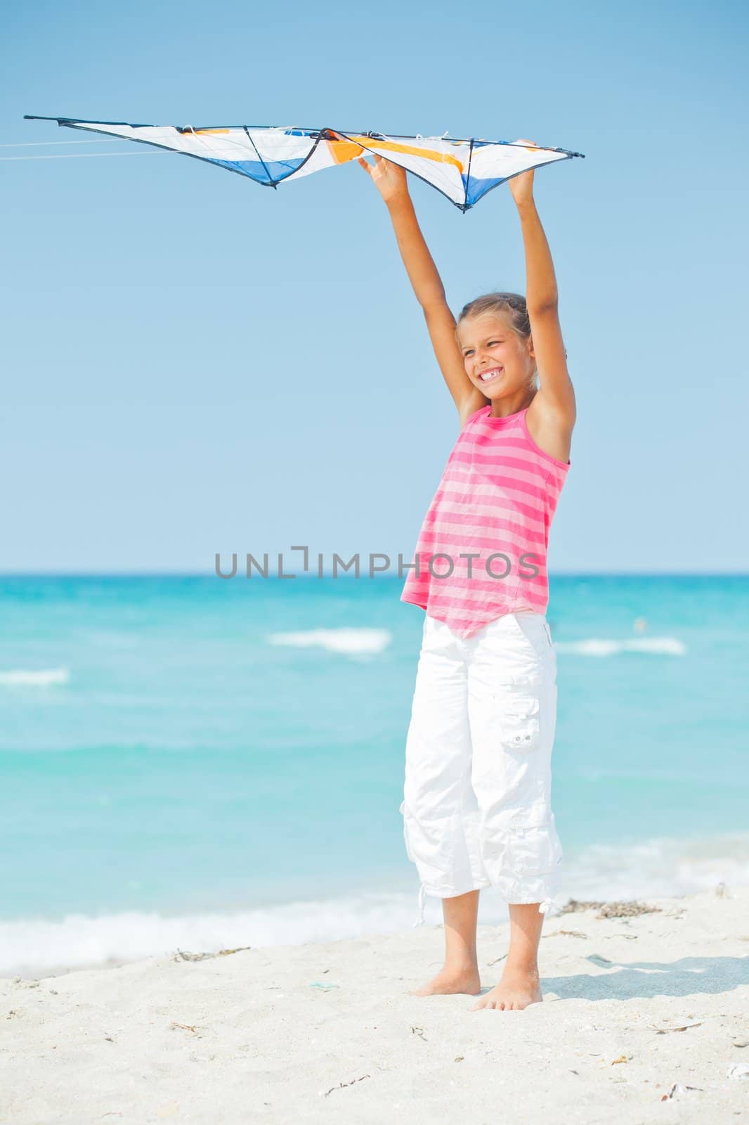 Young cute girl playing with a colorful kite on the tropical beach. Vertical view