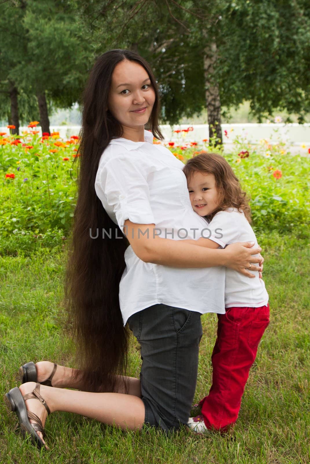 Double motherhood - pregnancy woman and her little daughter in a summer garden