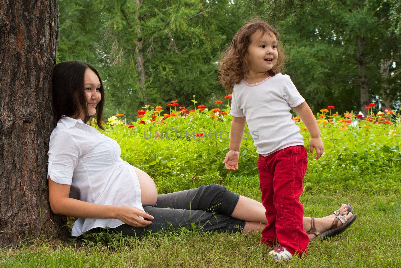 Young pregnant woman and her little baby girl in a summer garden