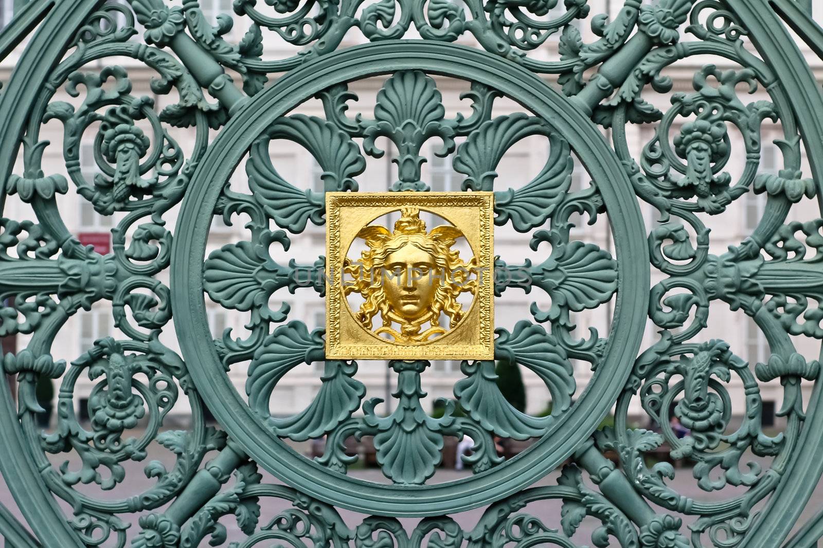 A green fence with a skillful metal pattern including a golden element in front of a palace in Torino