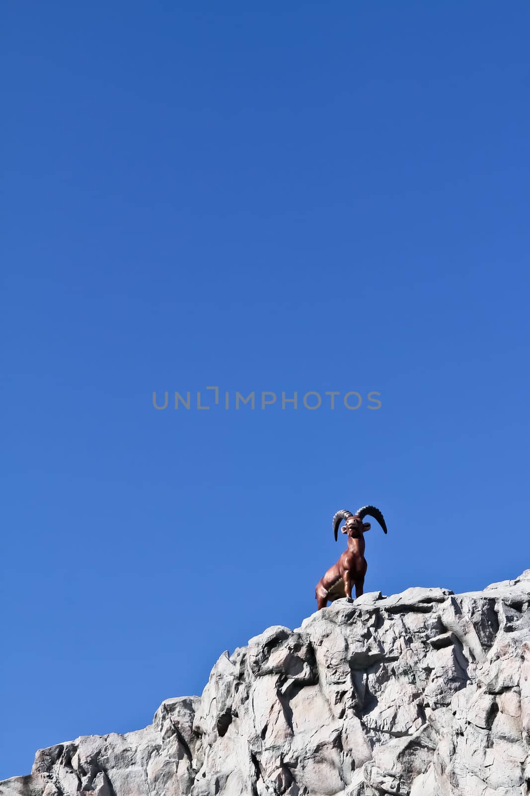 A fake capricorn on fake rock next to a ride in an amusement park in Vienna