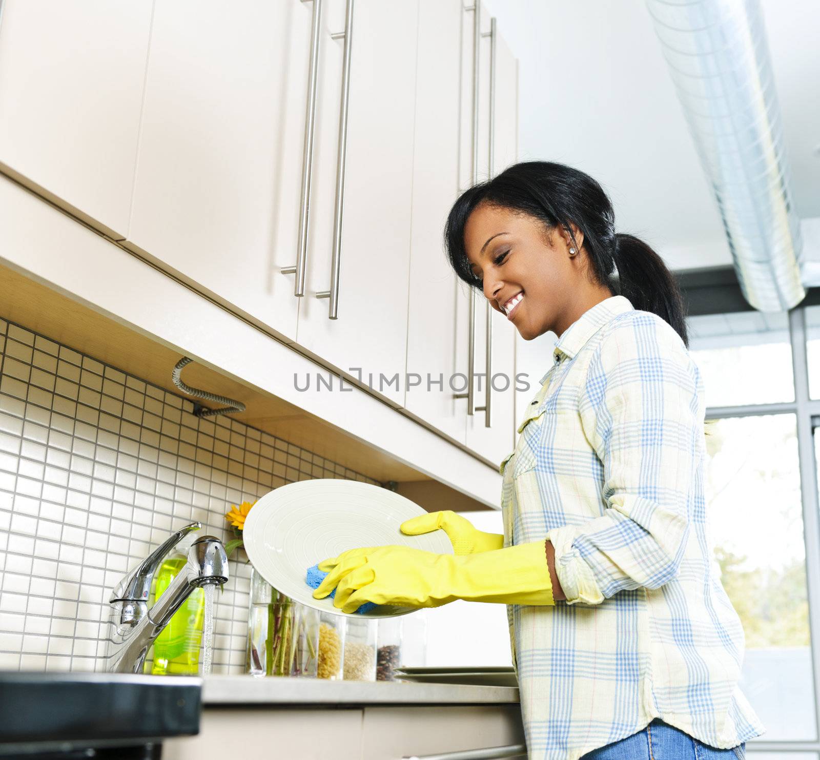 Smiling young black woman washing dishes in kitchen