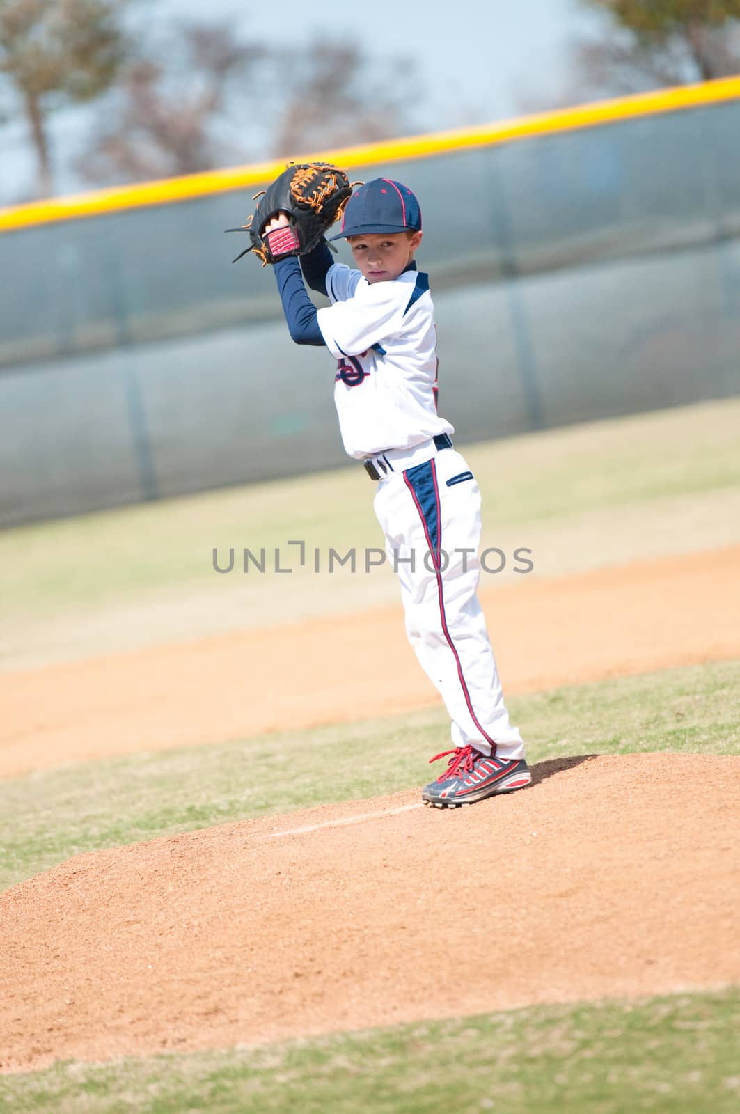Little league pitcher starting his wind up to pitch to the ball.