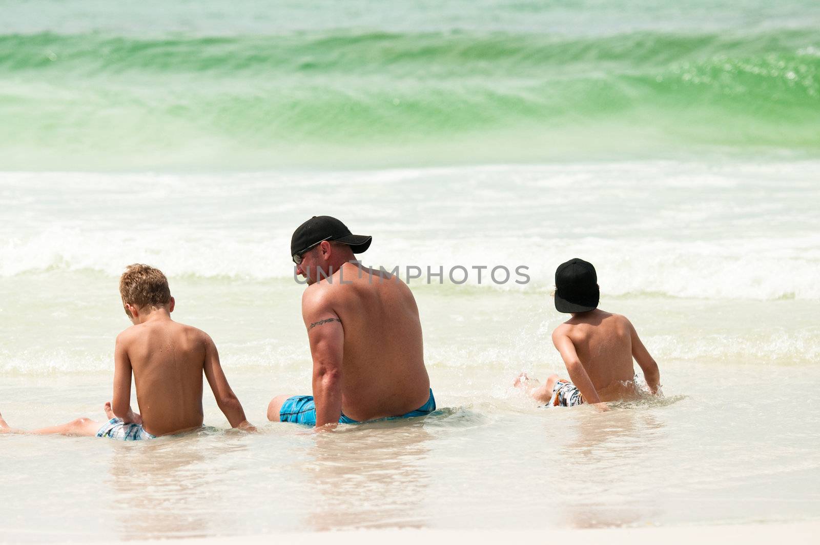 A dad and his boys sitting on the shore of the beach.