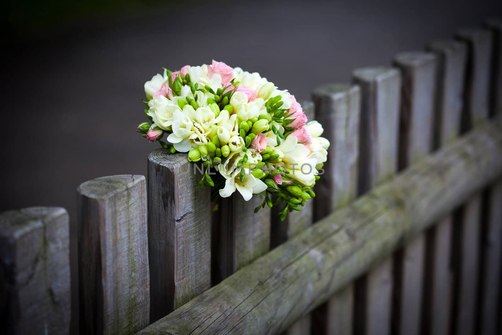 Wedding bouquet with roses and freesia on rustic country fence