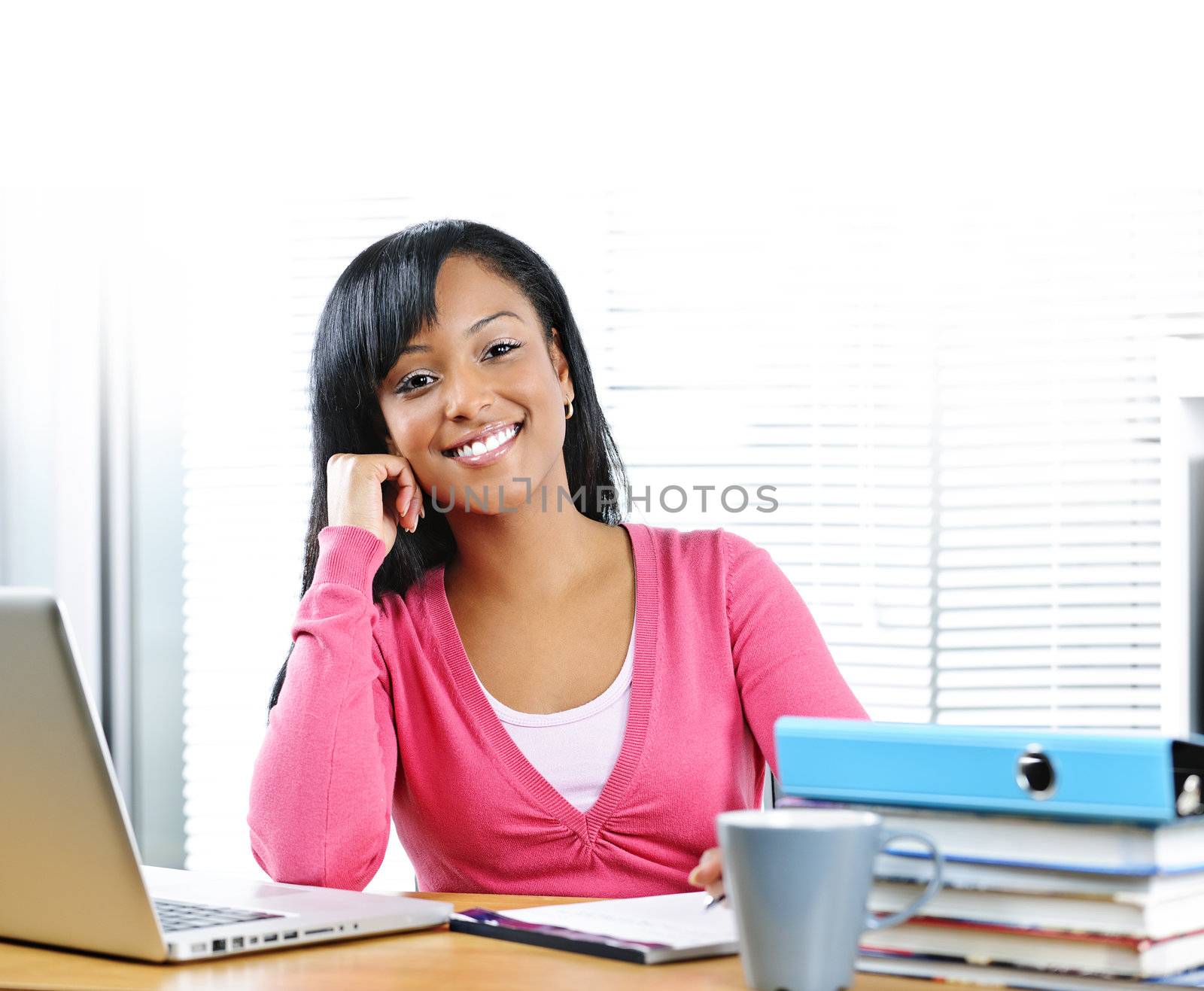 Smiling young black female student with computer and textbooks at desk