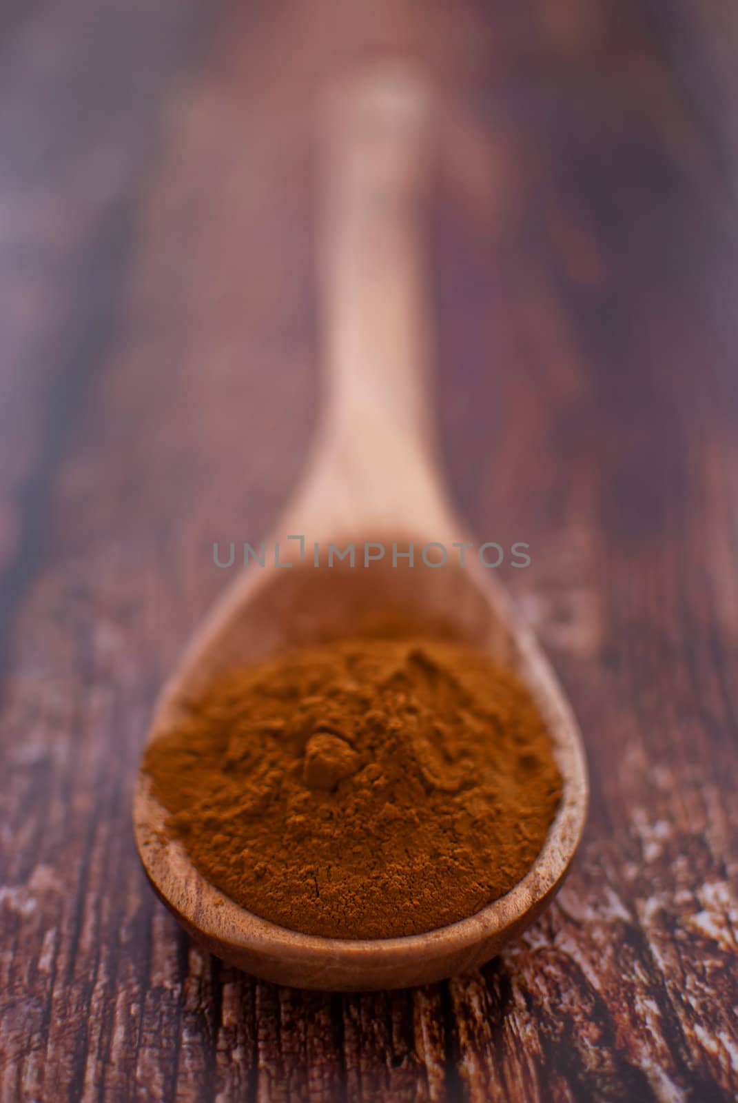 cinnamon powder in wooden spoon over wood background - selective focus