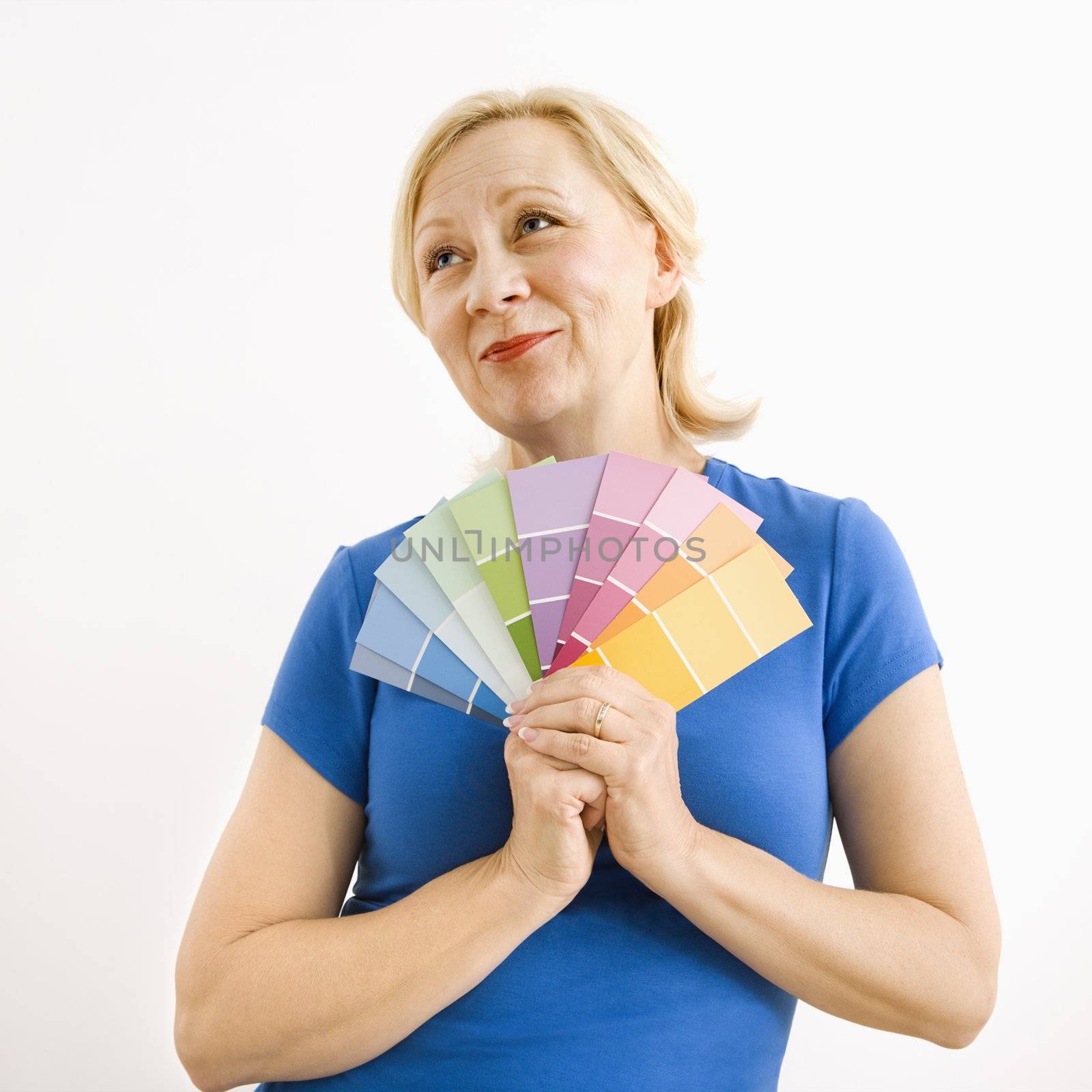 Portrait of smiling adult blonde woman holding paint swatches with hopeful expression.