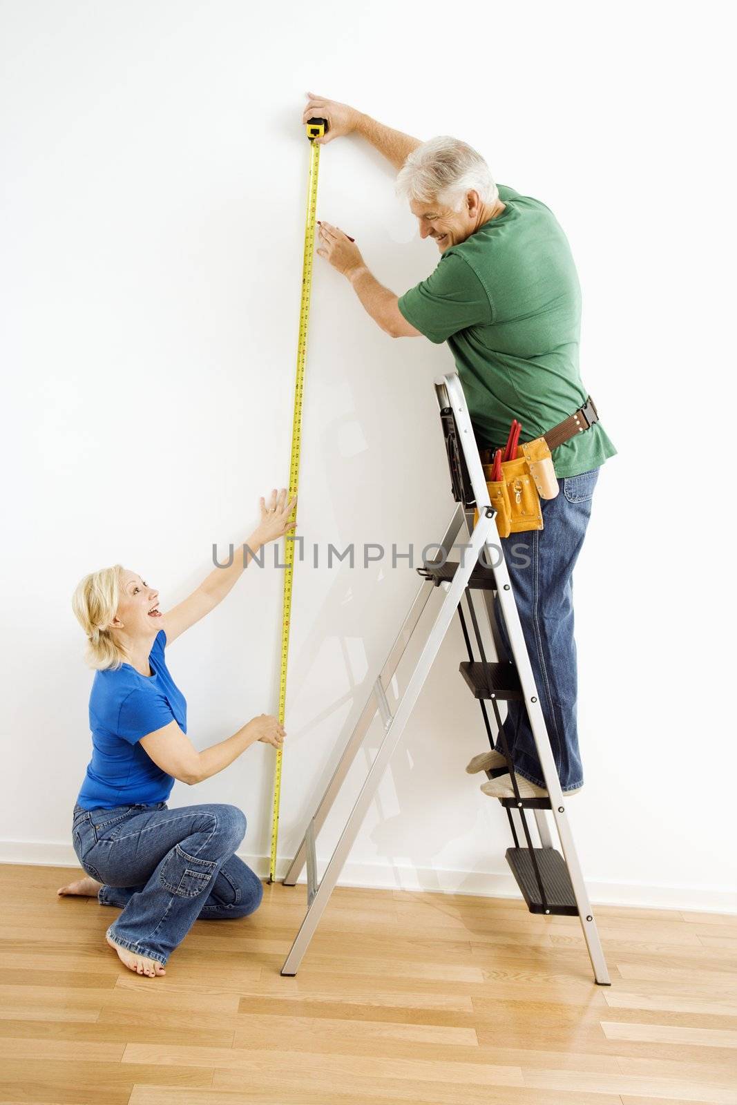 Man and woman measuring wall. by iofoto