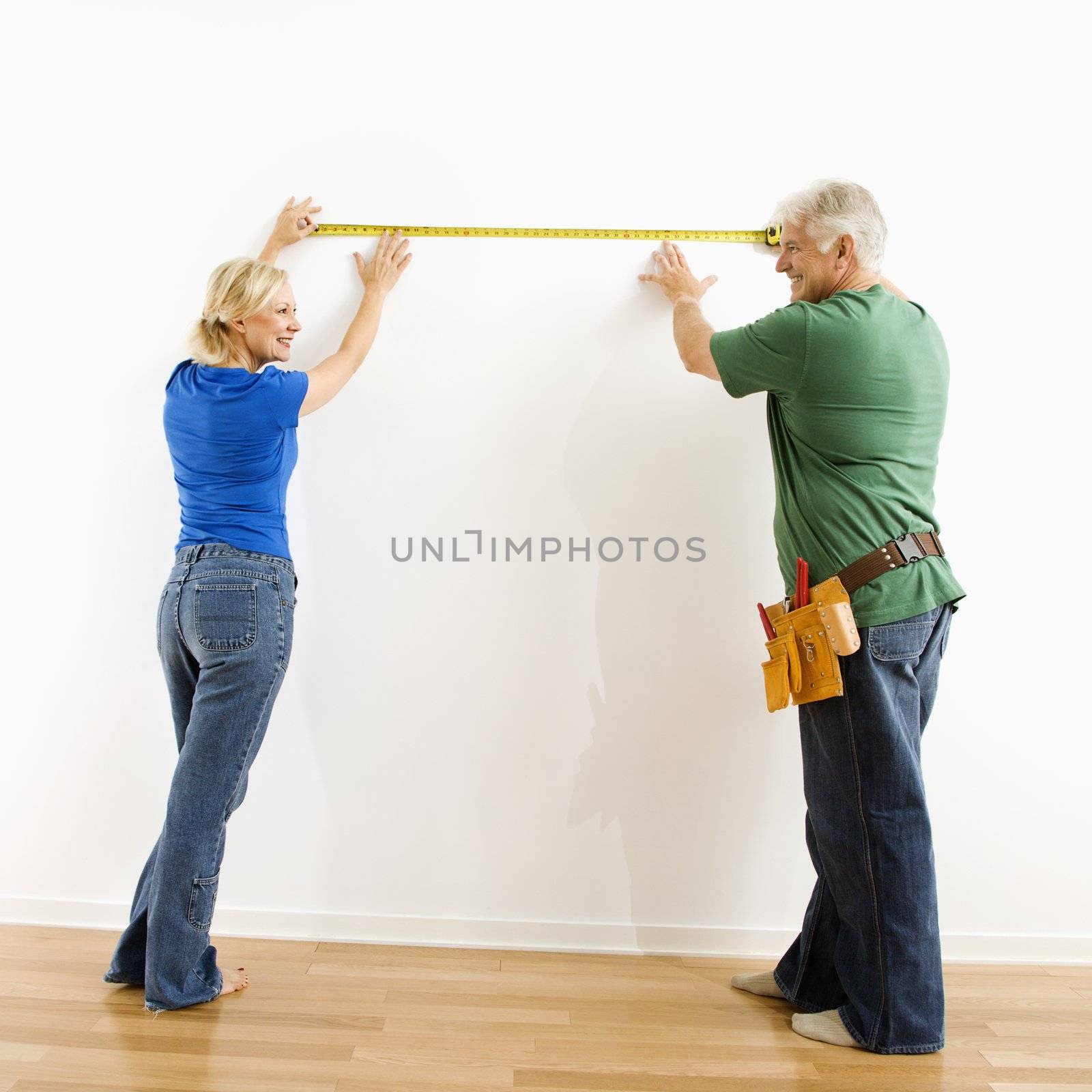 Man and woman measuring wall. by iofoto