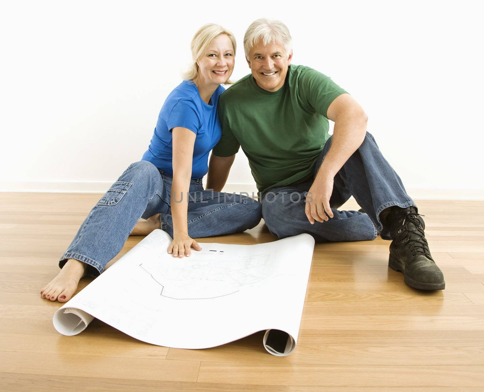 Middle-aged couple sitting on floor with architectural blueprints.
