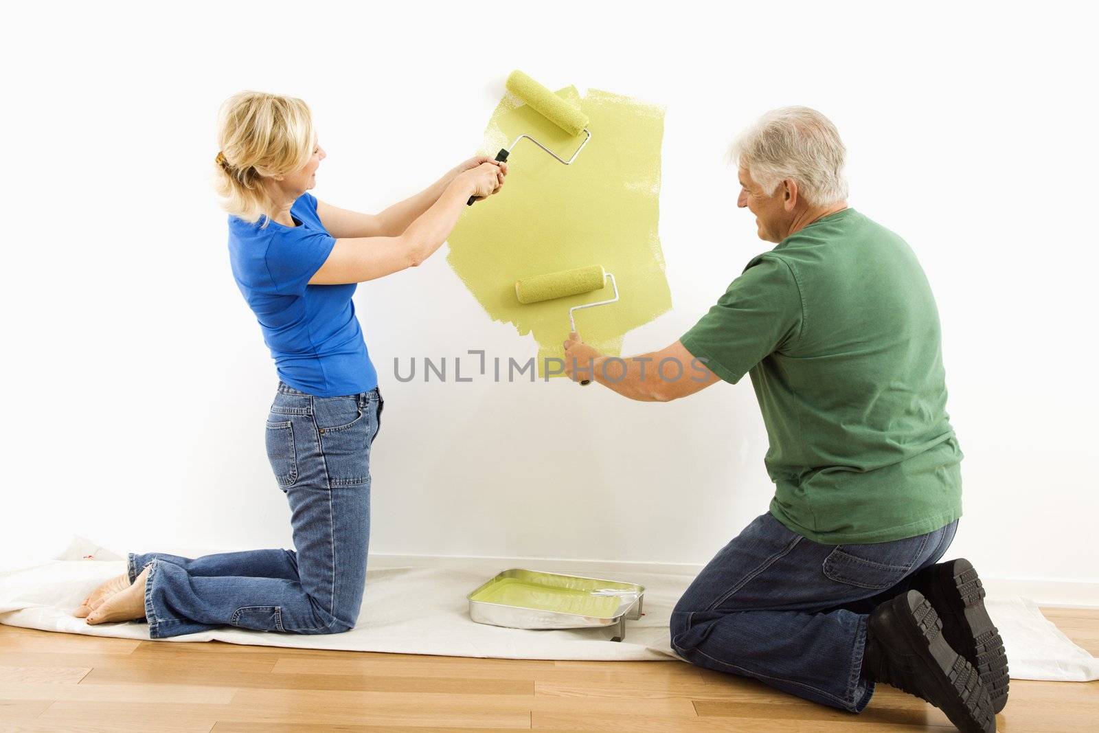 Middle-aged couple beginning to paint wall green over drop cloth.