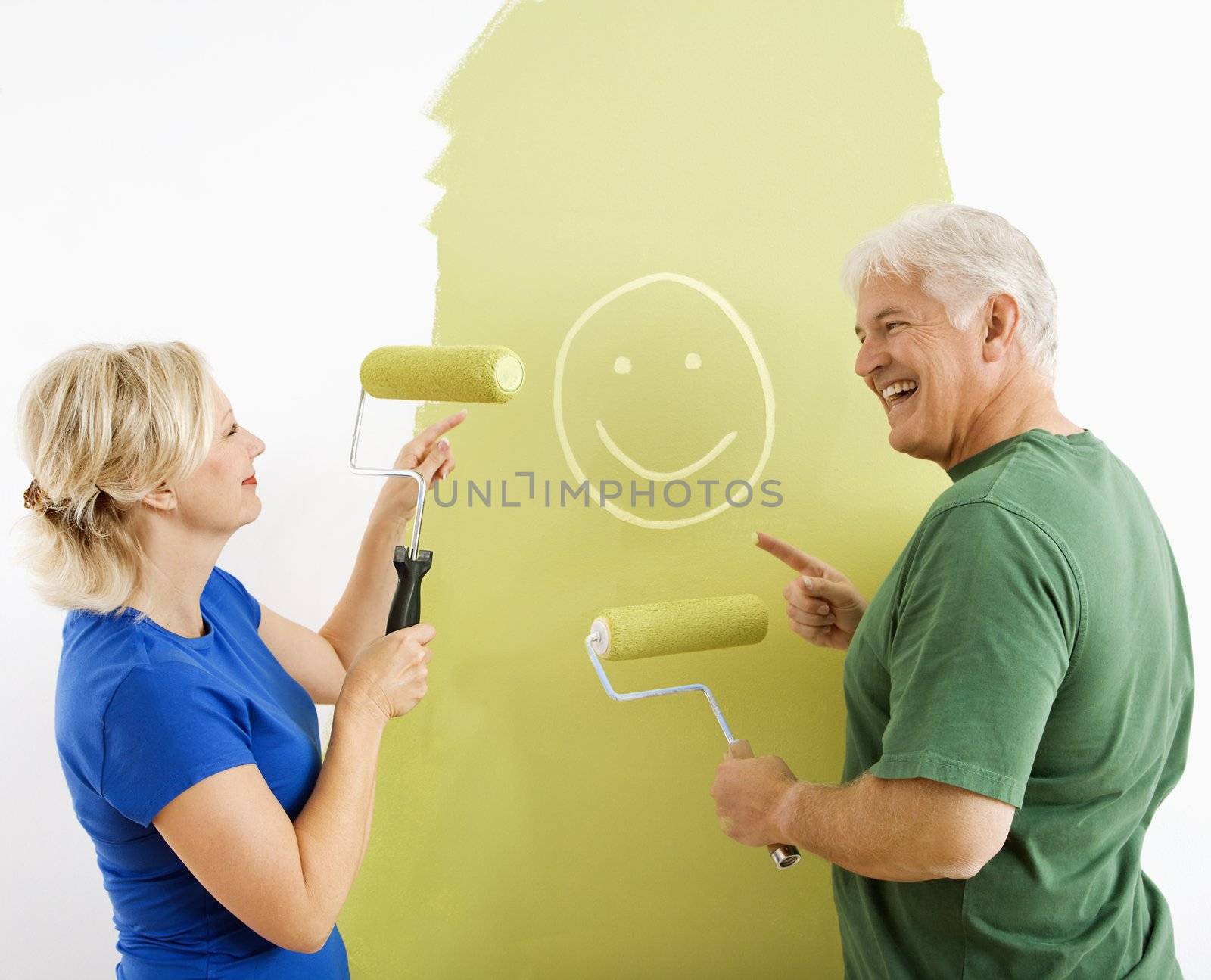Middle-aged couple painting wall green finger-painting smiley face for fun.
