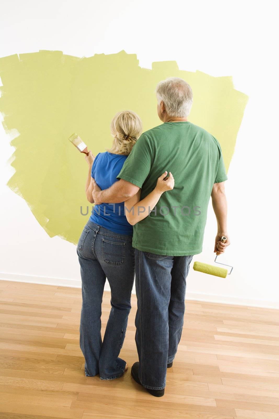 Middle-aged couple painting wall green observing their work.