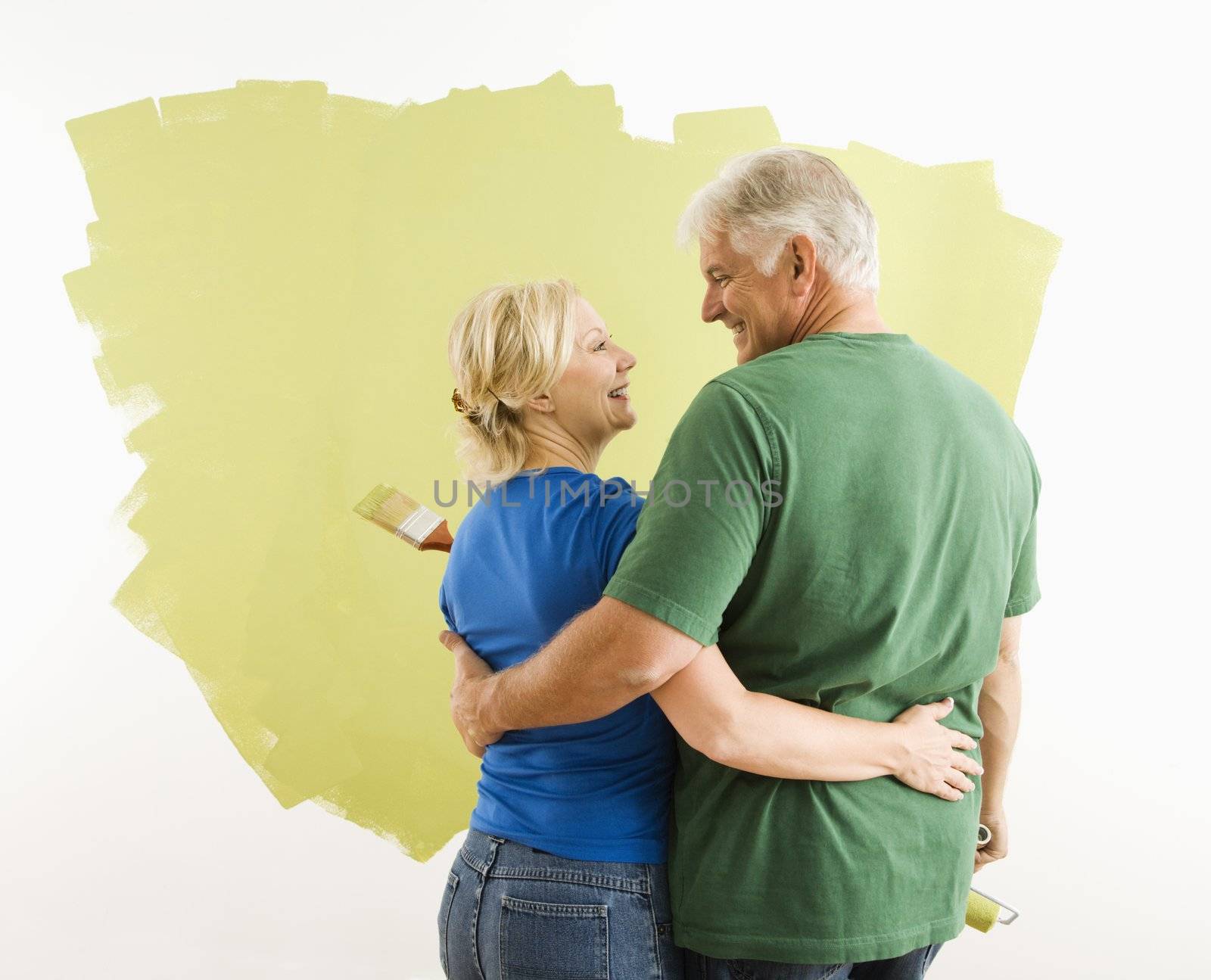 Middle-aged couple painting wall green observing and discussing their work.