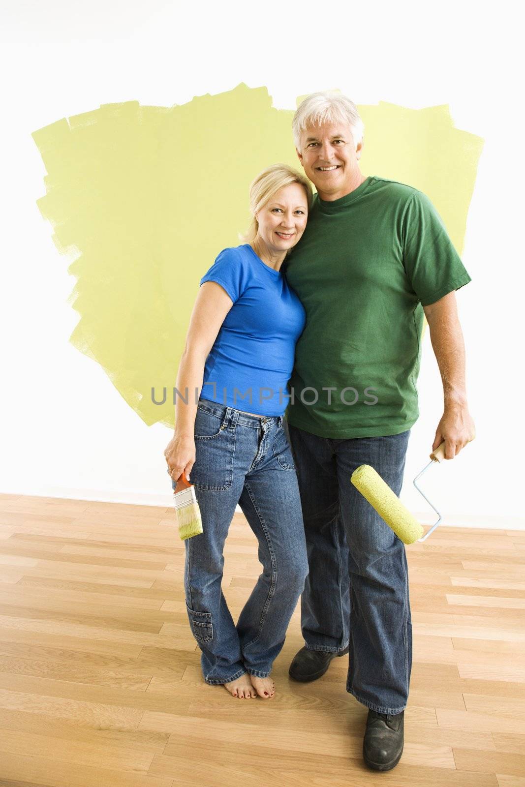Middle-aged couple in front of wall they are painting green.
