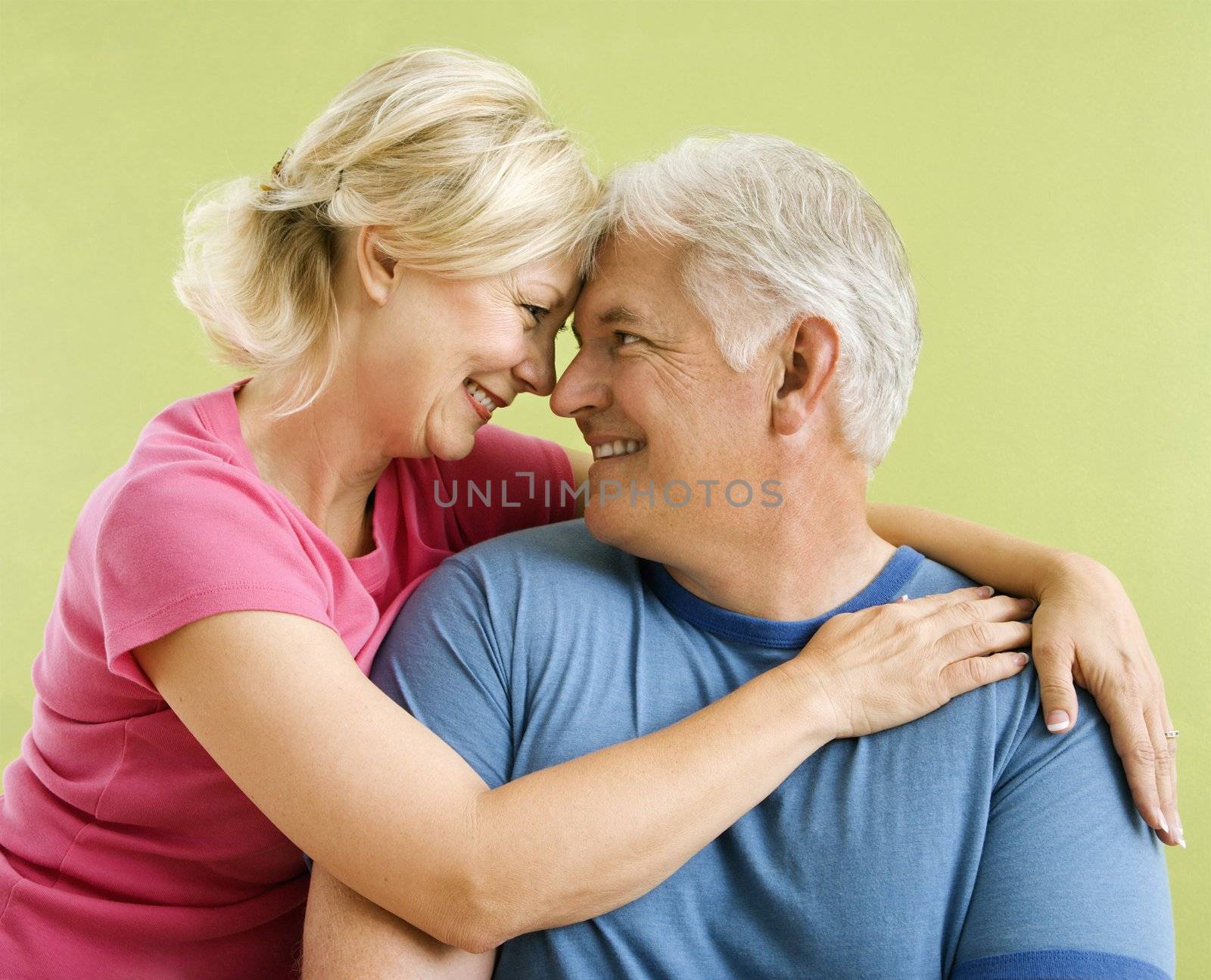 Portrait of smiling middle-aged couple in front of green wall snuggling.