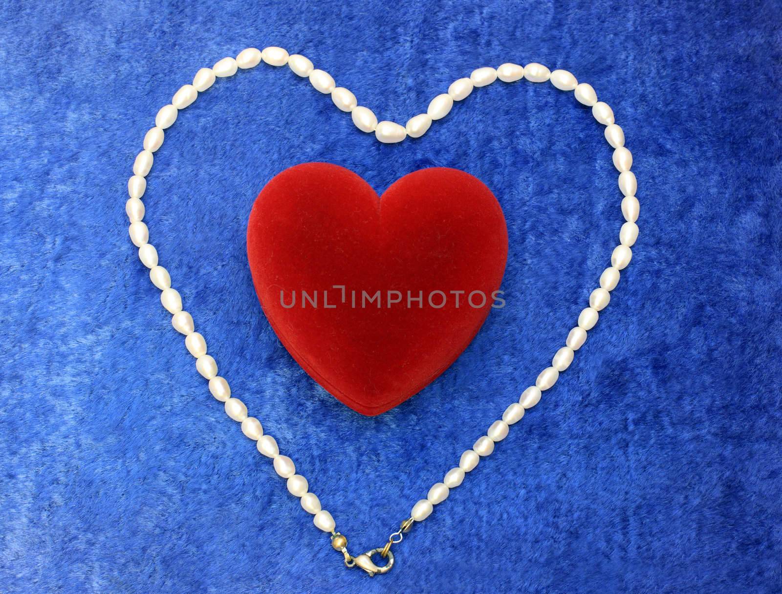 valentine's day composition: red heart and pearly neacklace on blue velvet