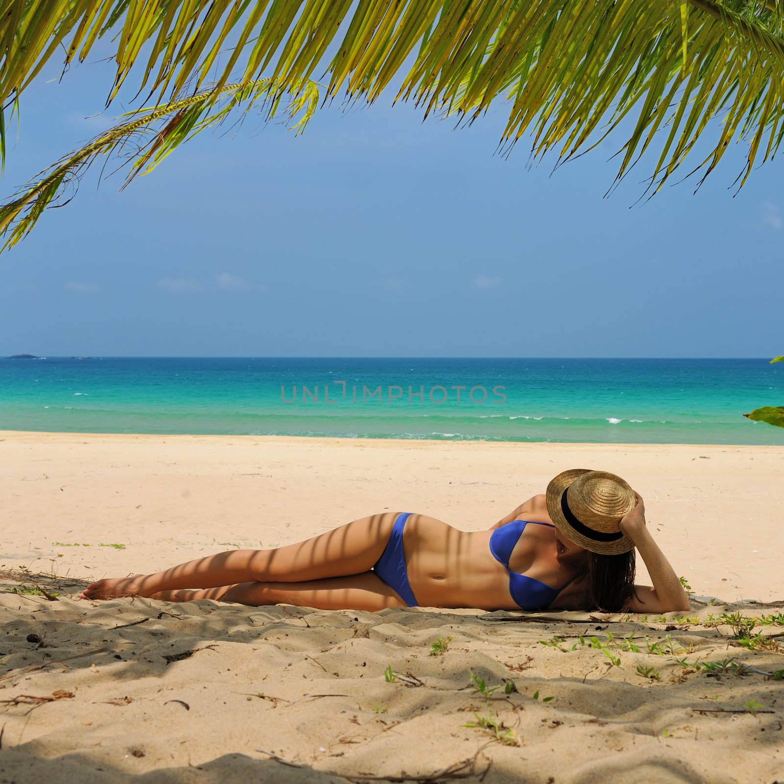 Woman at beach under palm tree with leaf shadow on her body