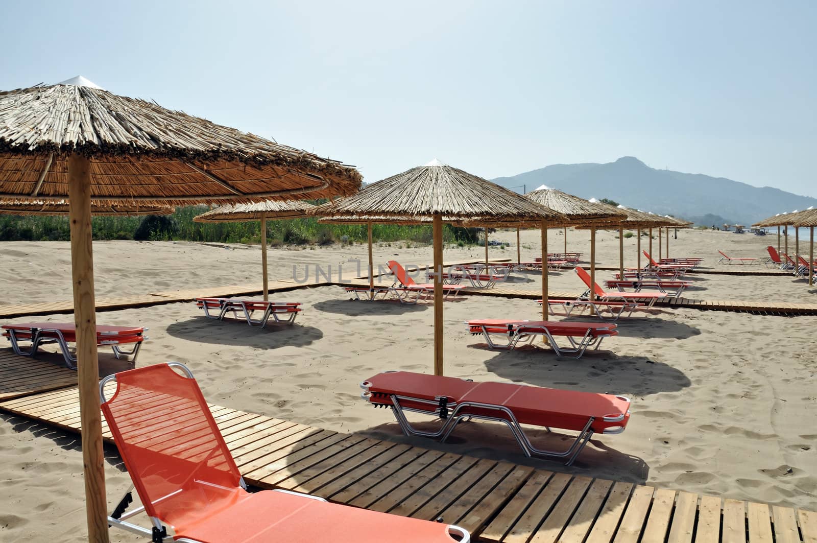 Rows of straw umbrellas and loungers at sandy beach Kalamaki Zakynthos, Greece.
