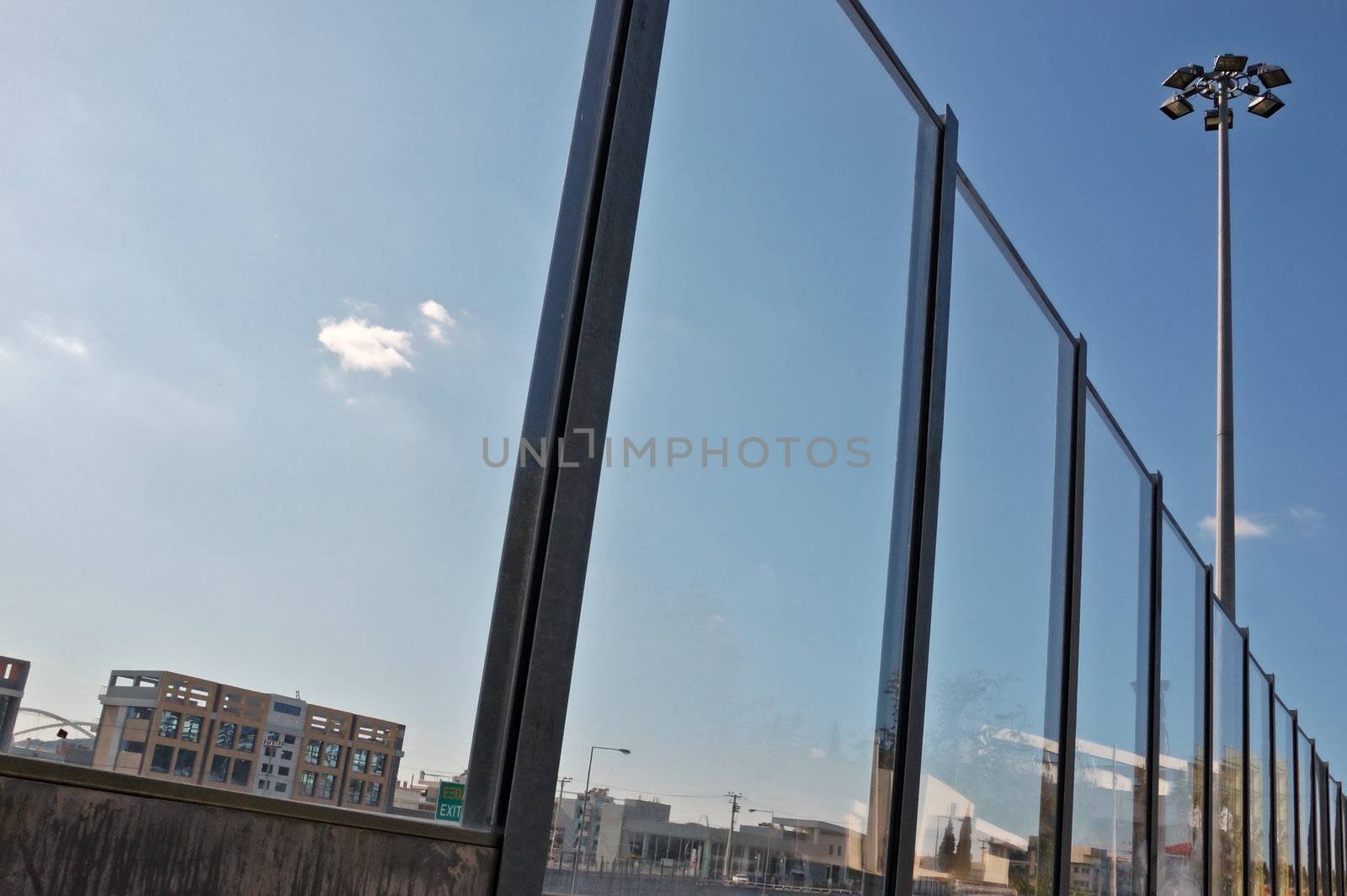 Distorted cityscape reflected on stained surface of highway traffic noise barrier.