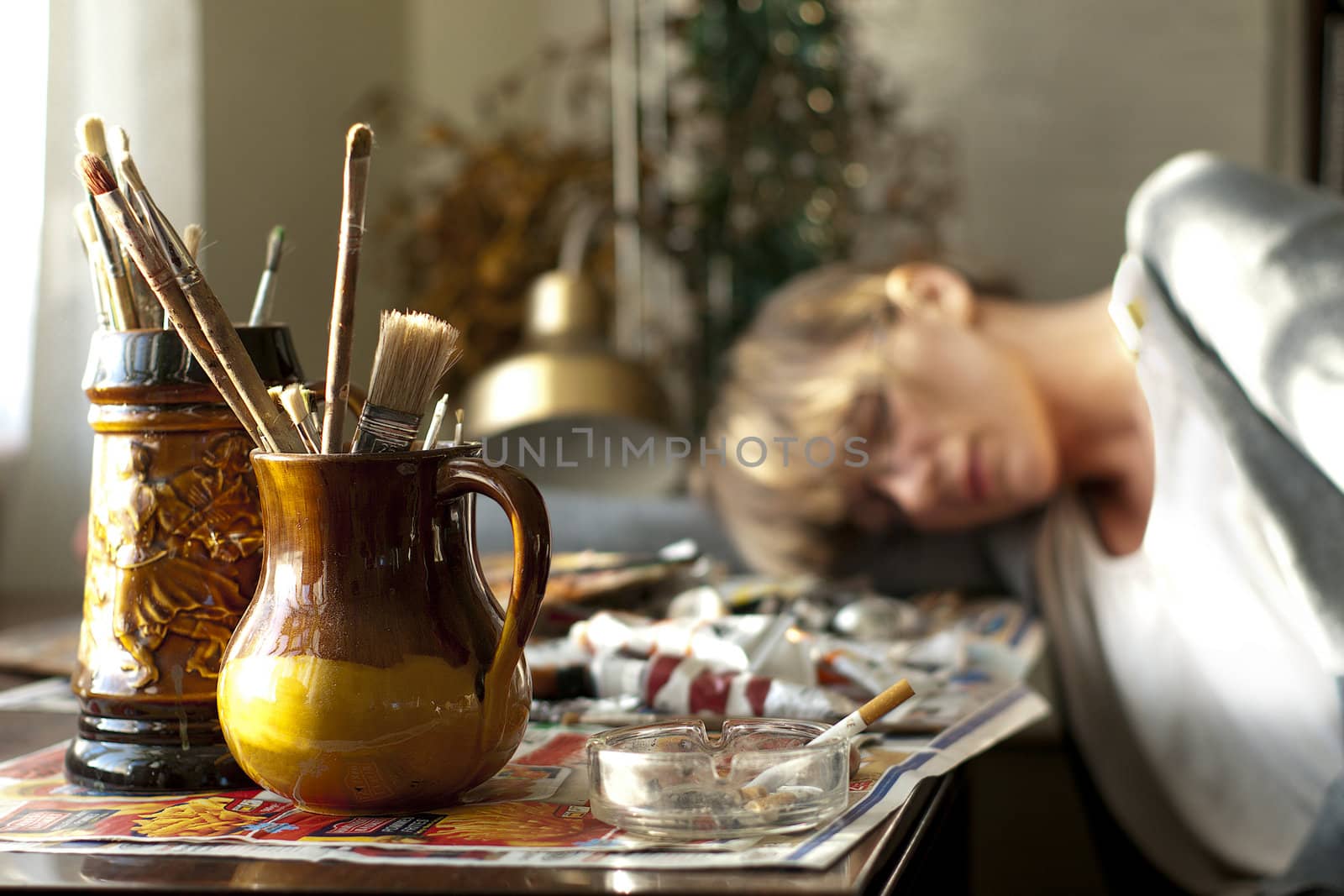 An artist sleeping on the table full of painting accessories.