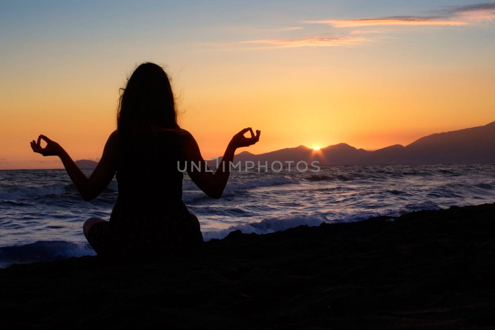 Silhouette of a young girl meditating at the beach.