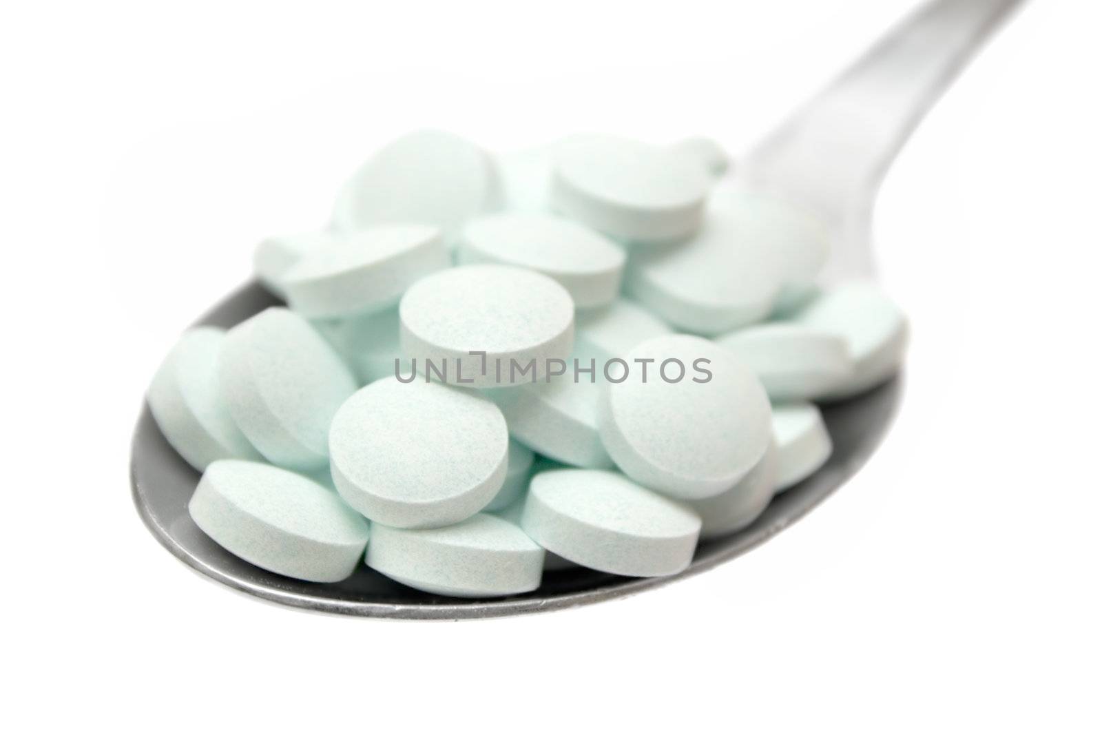 Greenish tablets on a silver spoon. Isolated on a white background.