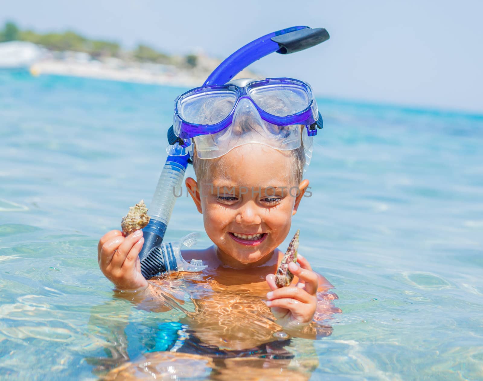 Portrait of young boy with seashells in snorkling equipment swimming in the transparent sea