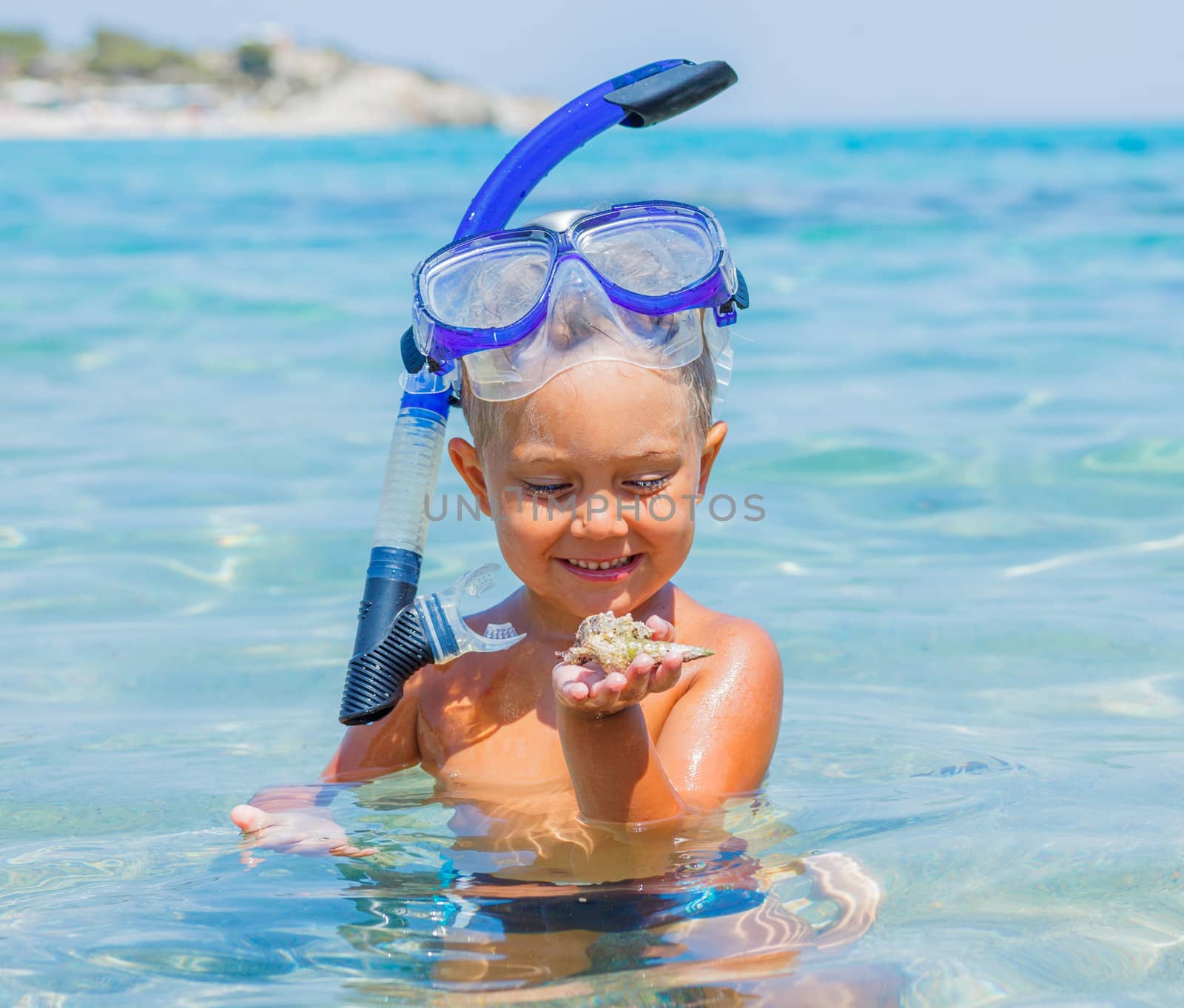 Portrait of young boy with seashells in snorkling equipment swimming in the transparent sea