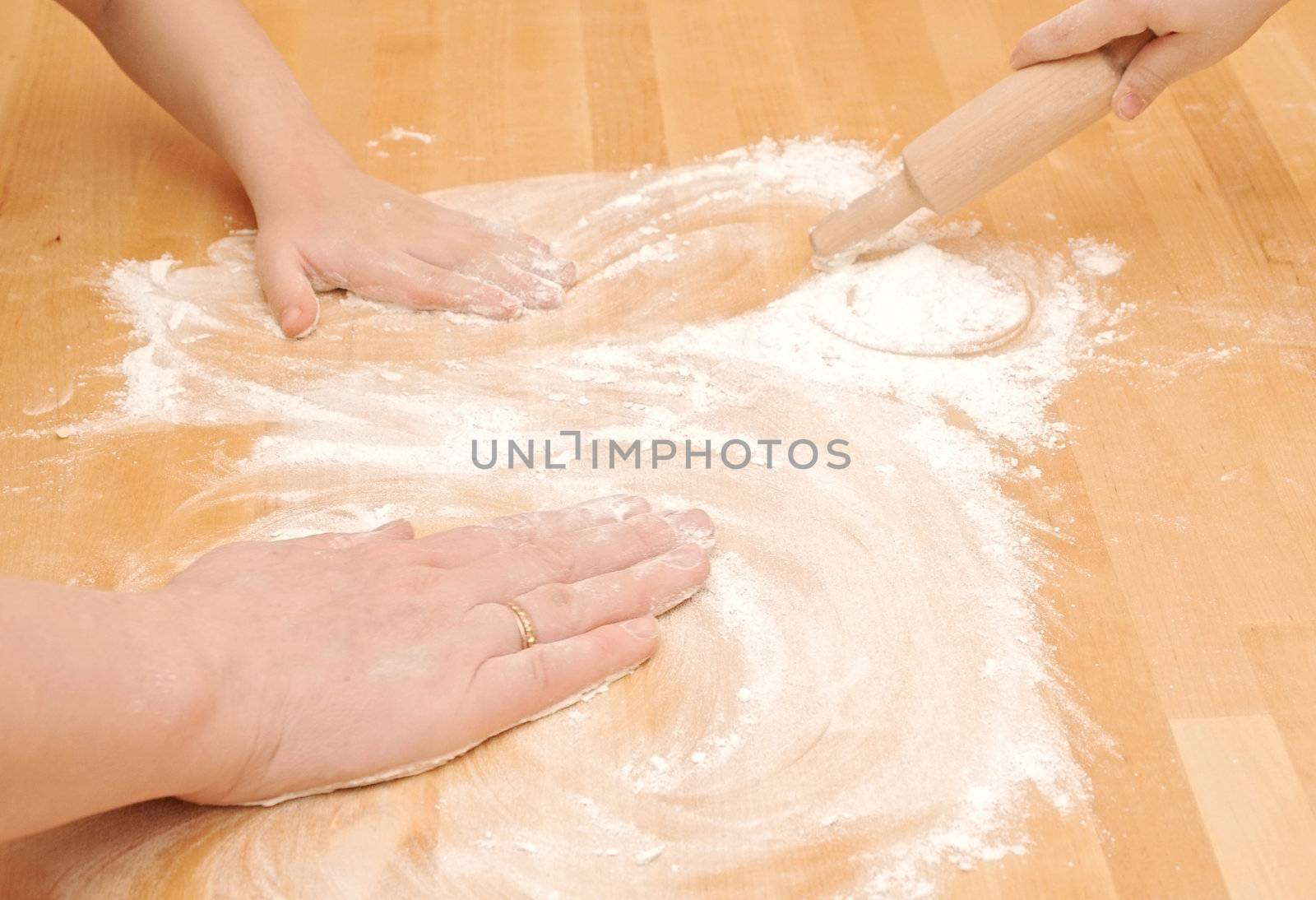 A child is helping mom to knead the dough for baking 