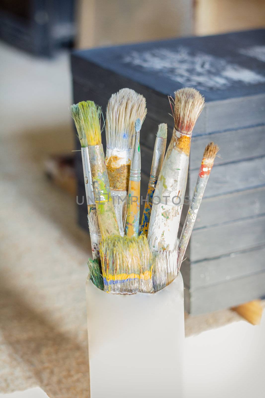 Set of paint brushes on jar, in front of artistic canvas