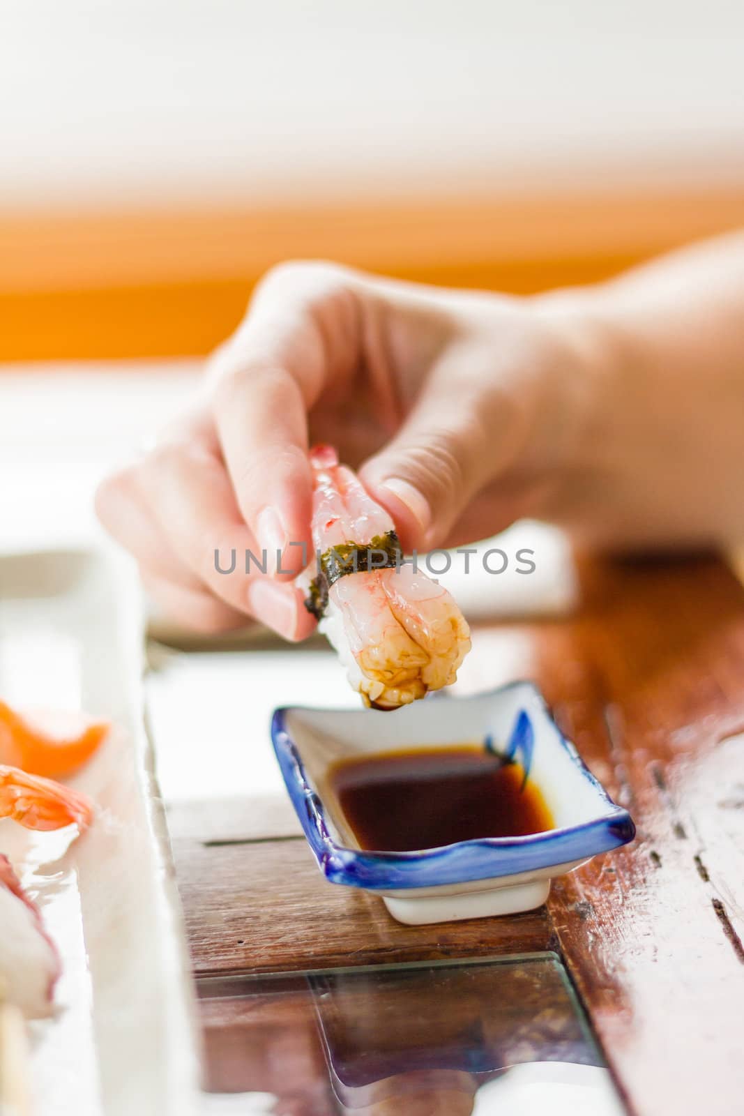 Closeup of hand girl dipping a piece of praw sushi on soya sauce with wasabi