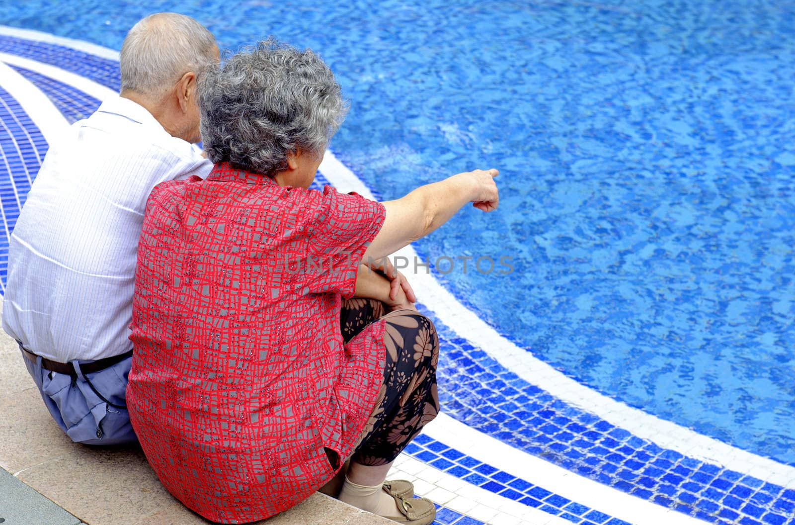 an intimate senior couple sitting beside a pool by jackq