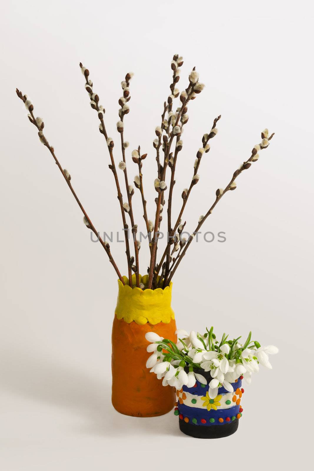 Spring still life with a bouquets of willows and snowdrops in the decorative plasticine vases on a light gray background.