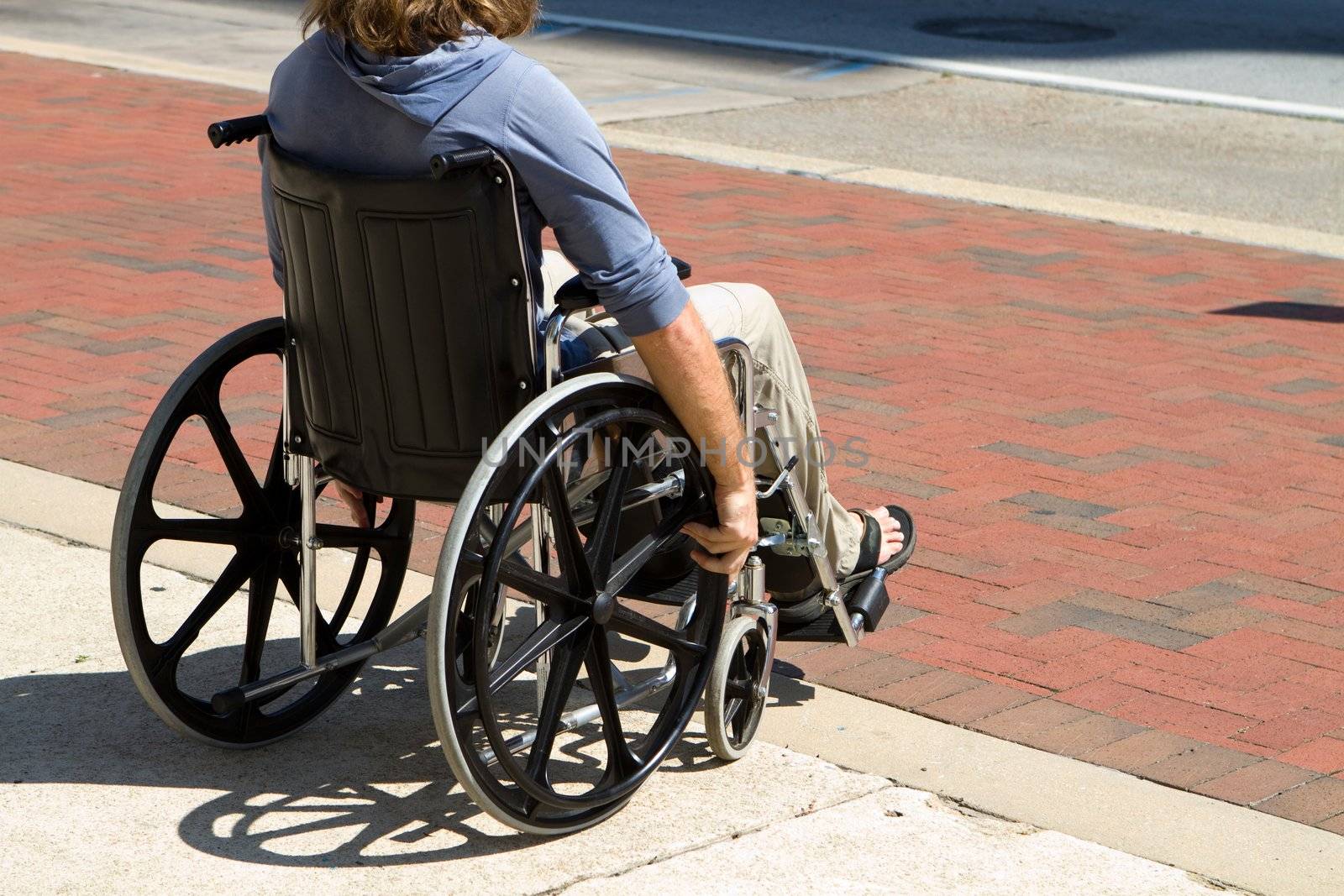 Injured male veteran sitting in his wheelchair rolls on the sidewalk.