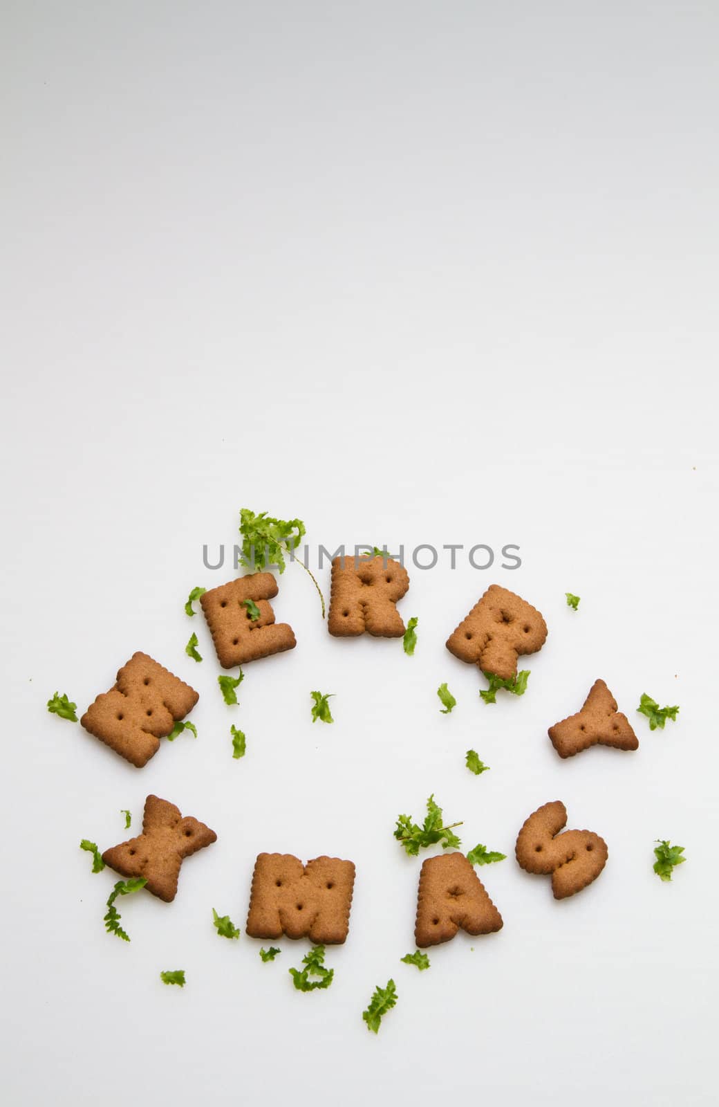 Merry Xmas wording from brown biscuits with green leaves on white background in portrait orientation