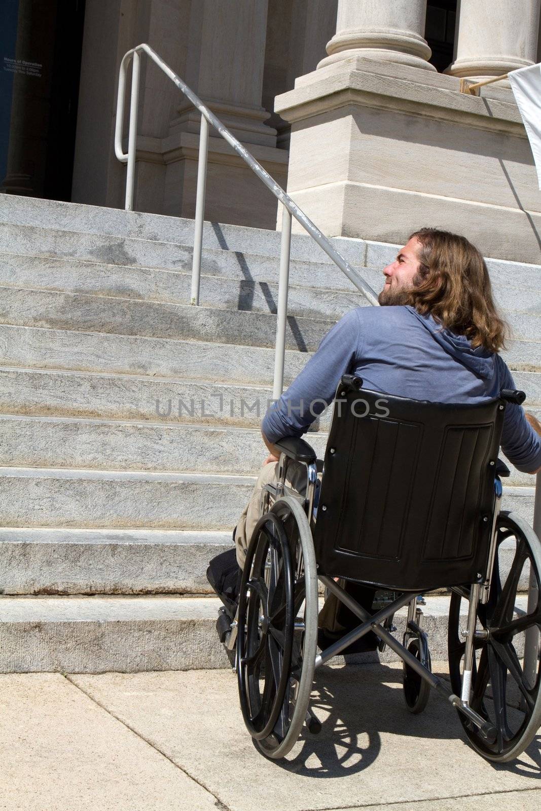 Disabled man in wheelchair looks for a ramp to gain access to a public building entrance.